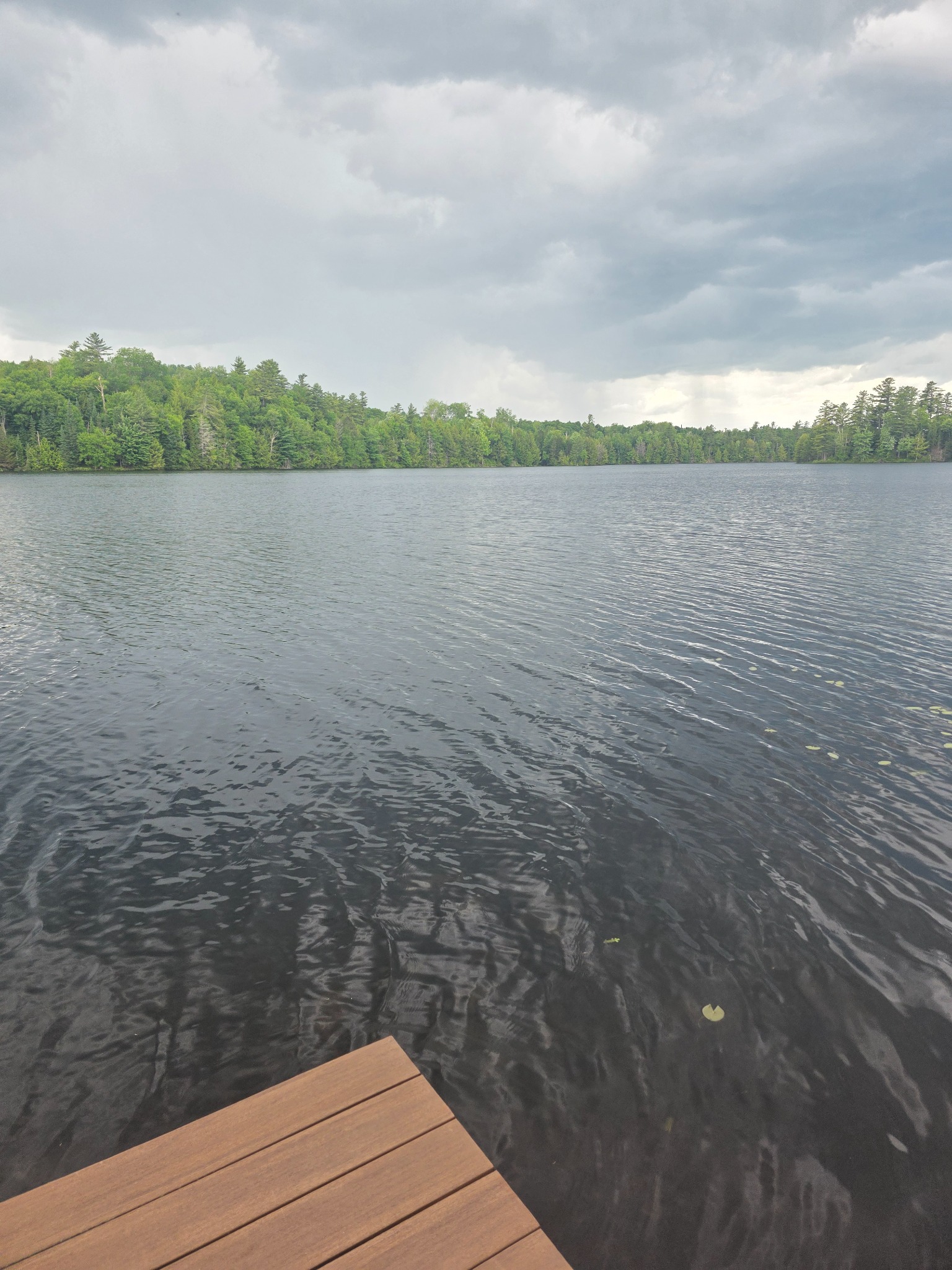 Dock edge, pond surface, and storm clouds lowering over the far shore