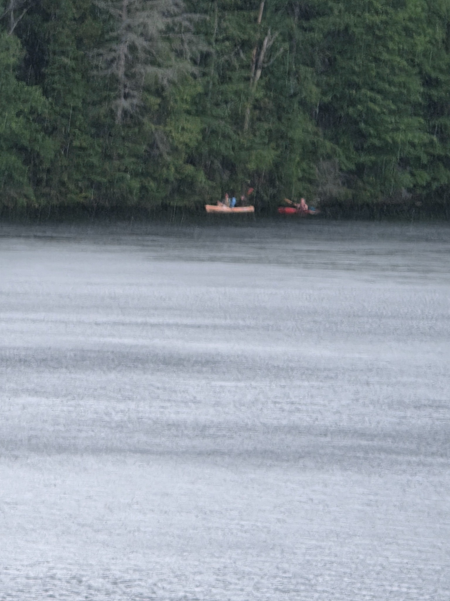 Distant kayakers moving along the far shore in heavy rain